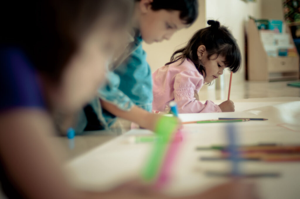 Three children working holding markers while working on paper.