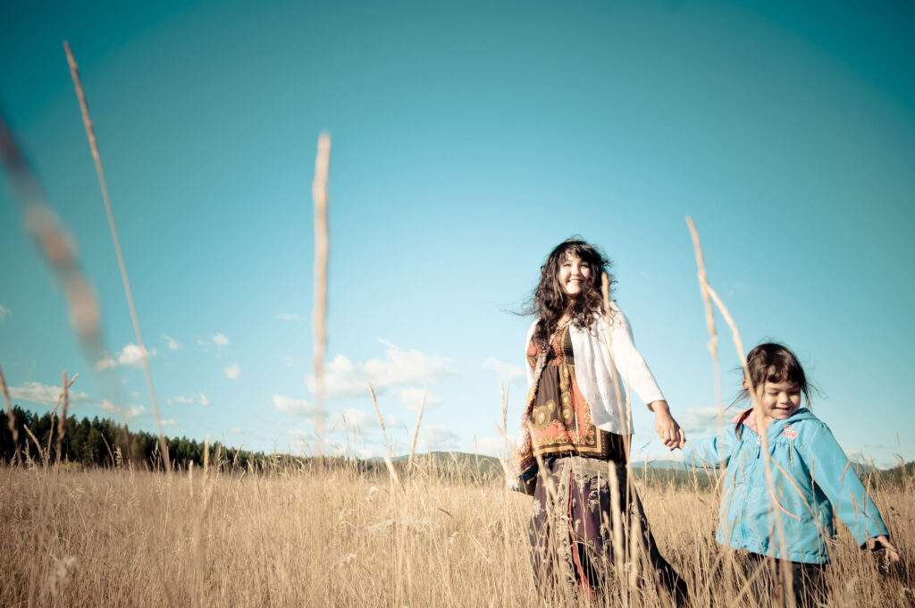 A woman and child stand in a field with blue sky in the background