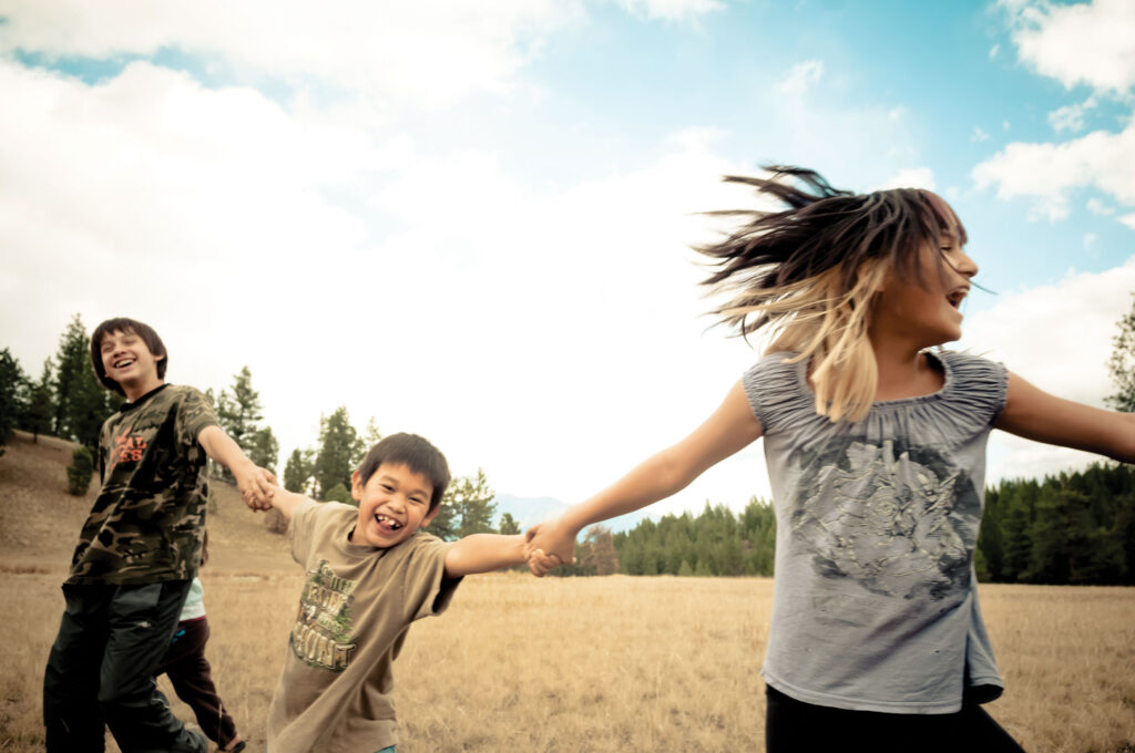 Three children holding hands as they laugh together in a field